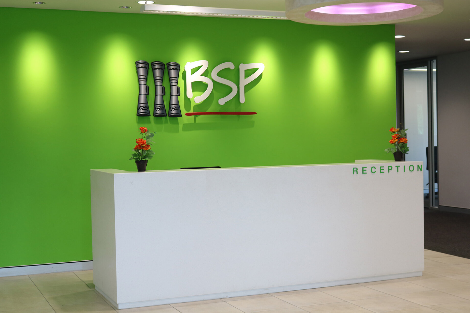 Interior of BSP building. A reception desk sits in front of a bright green wall with the BSP sign in the middle.